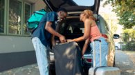 African american couple loading baggage in vehicle to leave on holiday vacation trip. Partners travelling by car with luggage, suitcase and bags to go to summer adventure cityscape.