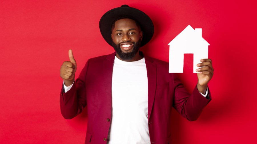 Real estate. Stylish african american bearded man showing home maket, thumb up, recommending agency or apartment complex, standing over red background.