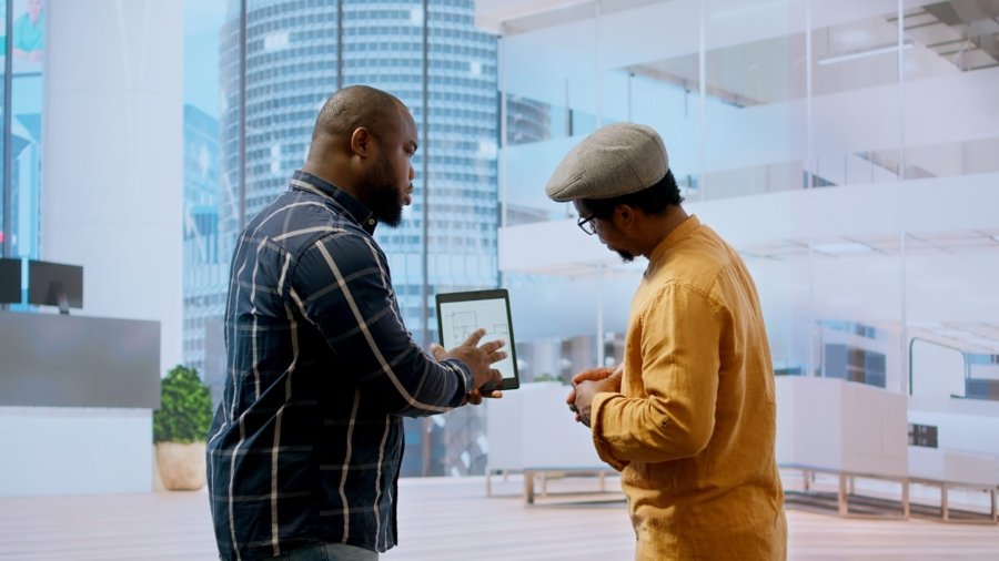 Real estate broker and client negotiating a leasing contract for a high class modern office space, evaluating blueprints on tablet during office tour. Property investment opportunity. Camera A.