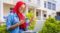A beautiful young African woman smiling while using her laptop outside