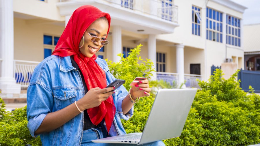A beautiful young African woman smiling while using her laptop outside